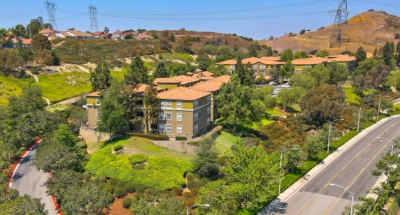 aerial view of residential building, surrounding streets, and hills in background, taken on a sunny day