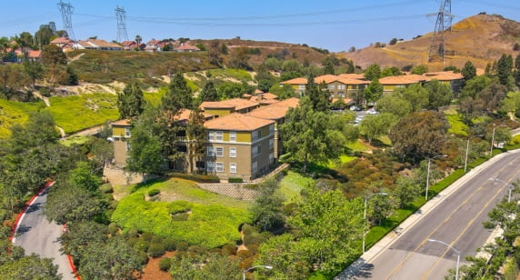 aerial view of residential building, surrounding streets, and hills in background, taken on a sunny day